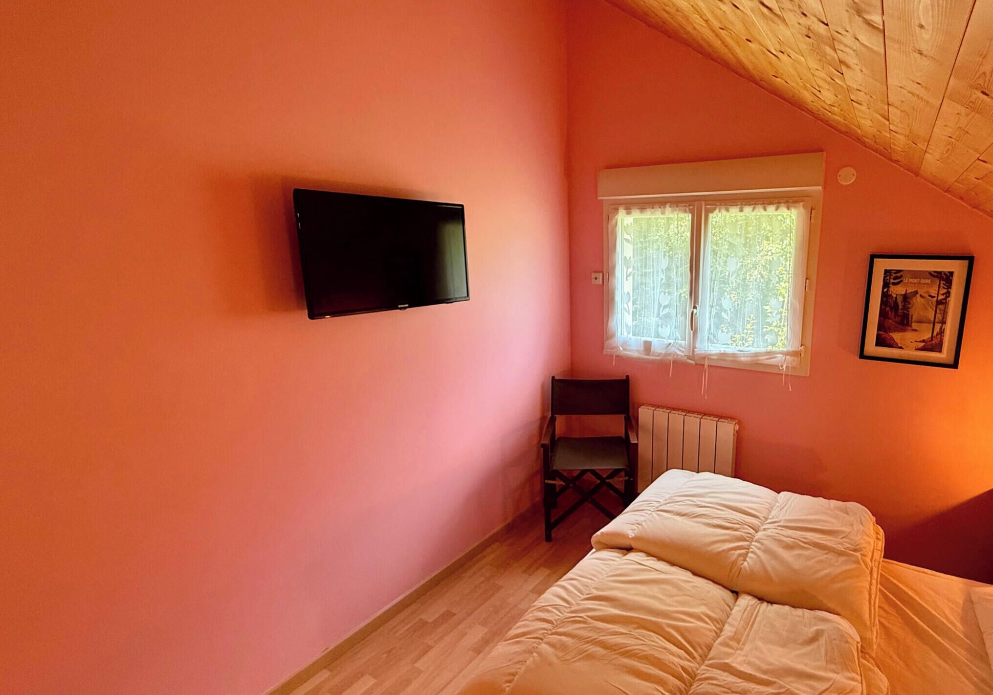 A bedroom with a bed, a chair, a television, a window with curtains, and a radiator.