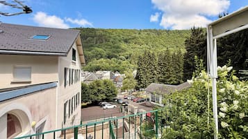 A residential area with a building featuring a balcony, a parking lot, and a view of a forested hillside.