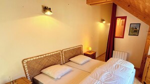A bedroom with two beds, wooden headboards, a nightstand with a lamp, a radiator, and a wooden dresser. - La Pergola Le Mont Dore (6 people) (Mont-Dore)