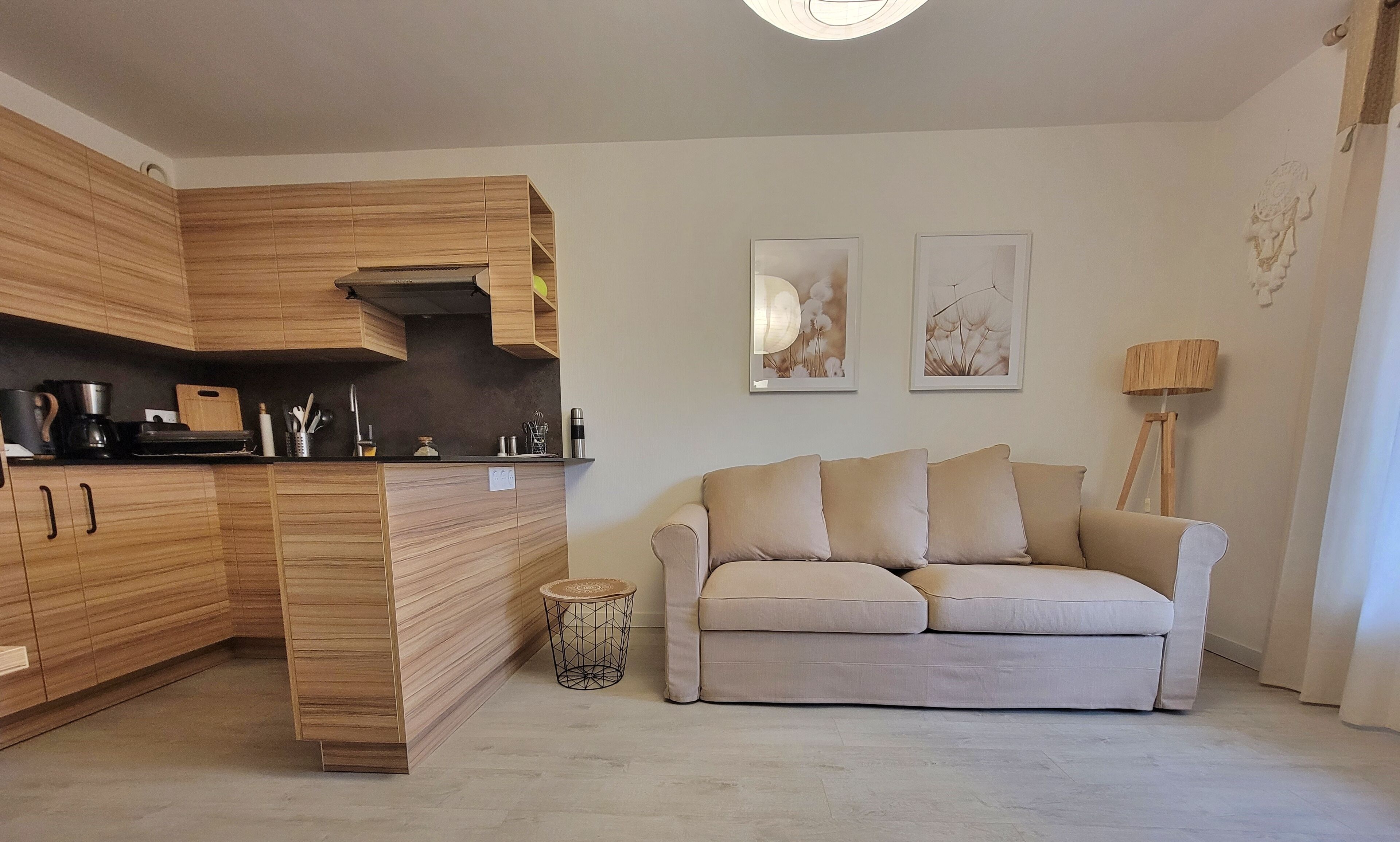 A modern kitchen with wooden cabinets, a built-in stove, and a dining area with a beige sofa and a floor lamp.