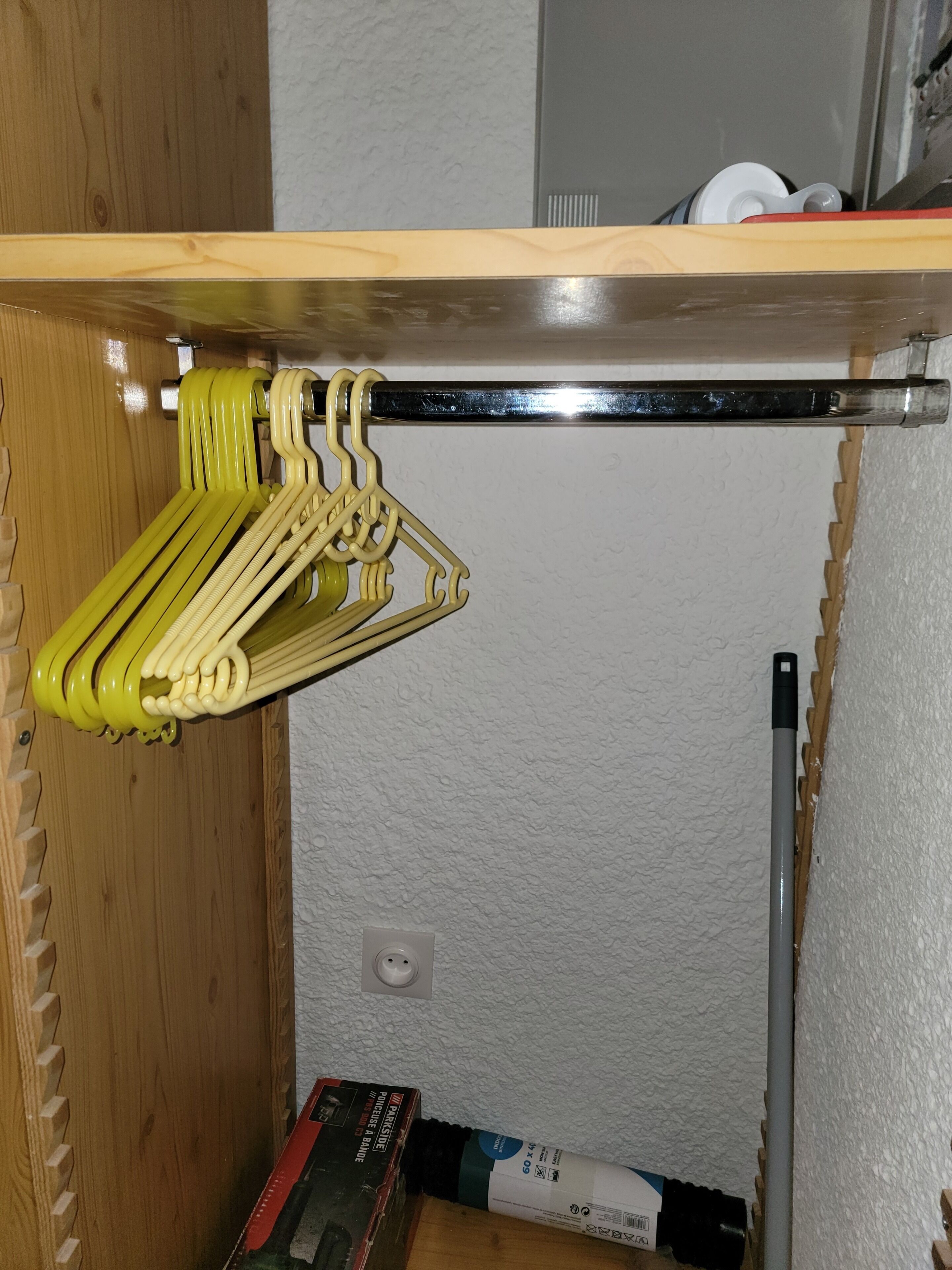 A wooden shelf with a metal rod, a yellow hanger, and a box labeled 'DANGER' on the floor.