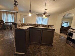 A kitchen with a dark island, hanging pendant lights, and a view into the living room.