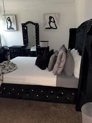 A bedroom with a bed, pillows, a dresser, a mirror, and artwork on the wall.