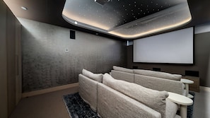 Ein Heimkino mit großer Leinwand, bequemen Sitzgelegenheiten und ansprechendem, modernem Deckenstil.