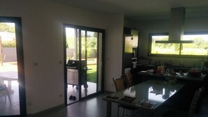 Une cuisine moderne avec un coin repas, de grandes fenêtres et une porte-fenêtre coulissante donnant sur un patio.