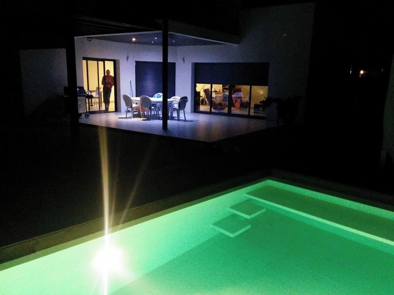 An indoor space with a green-lit floor, a person standing near a door, and a table with chairs.