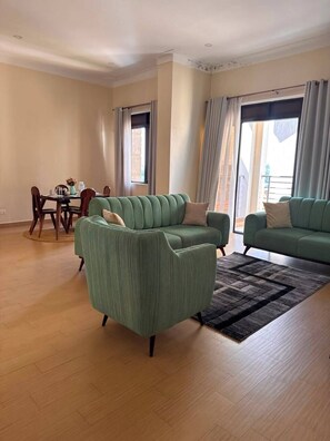 A living room with two green sofas, a dining table with chairs, and large windows with curtains. - Lovely 3-bedroom apartment in peaceful Kampala neighborhood (Kampala)