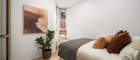 A bedroom with a bed, a potted plant, a chair, and a painting on the wall.