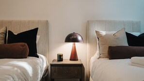 Ein Hotelzimmer mit zwei Betten, jeweils mit Kopfteil, einem Nachttisch mit Lampe und einem kleinen dekorativen Gegenstand auf dem Tisch.