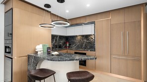 A modern kitchen with a marble countertop, wooden cabinets, and a built-in island with bar stools. - The Elara, Neutral Bay Isyd (Neutral Bay)