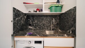 A compact kitchen with a marble backsplash, a stainless steel sink, and a built-in washing machine.