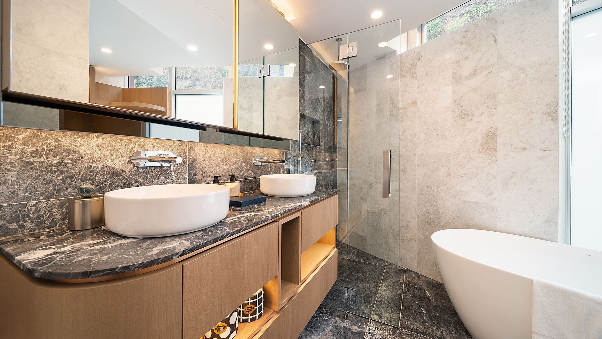 Un baño moderno con un espejo grande, dos lavamanos, una bañera y una ducha con mampara de vidrio.