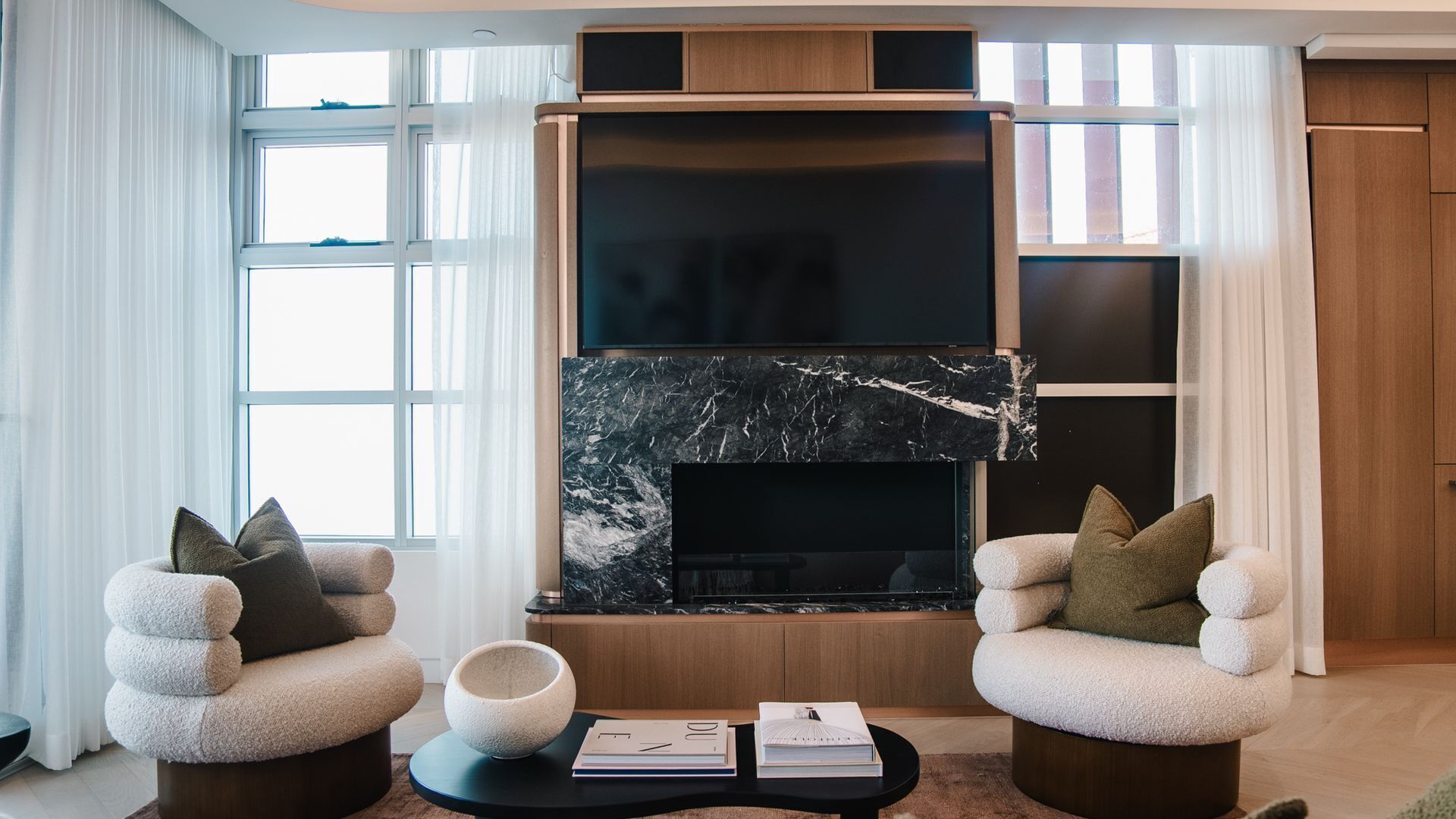 A modern living room with a fireplace, two plush armchairs, a coffee table, and a bookshelf.