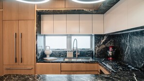 A modern kitchen with a marble countertop, stainless steel sink, and a red mixer.