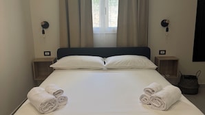 Un lit bien fait, avec du linge de lit blanc, deux tables de chevet avec des lampes et une fenêtre avec des rideaux.