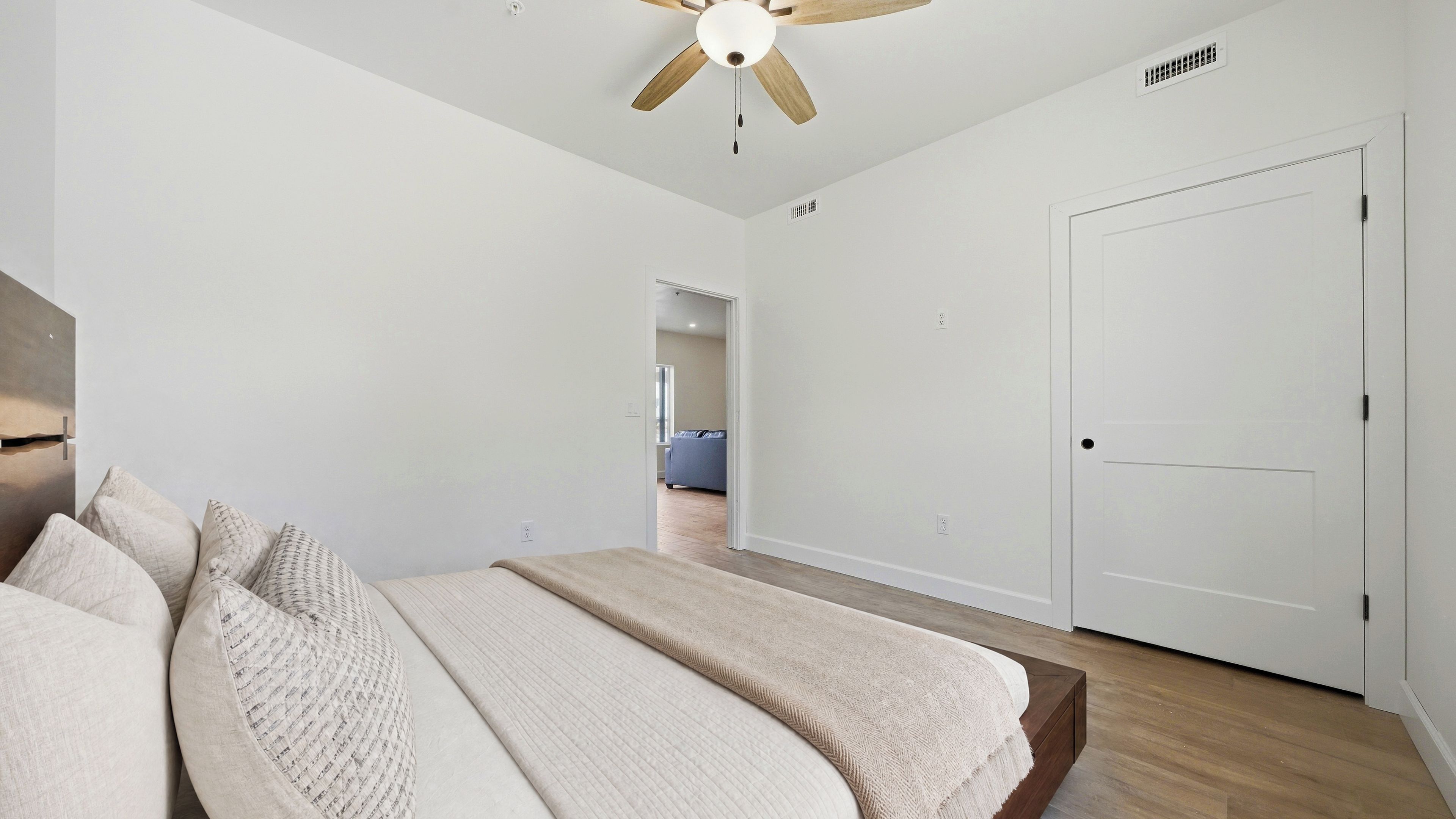 Un dormitorio con una cama, un ventilador de techo, una puerta y un pasillo que conduce a otra habitación.
