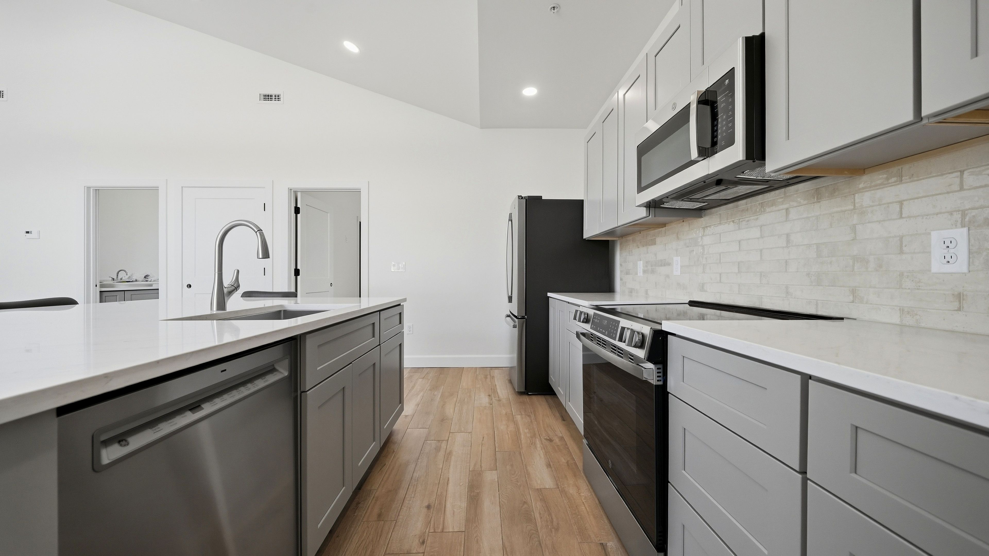Une cuisine moderne dotée d’appareils électroménagers en acier inoxydable, de meubles blancs et d’un plancher en bois.