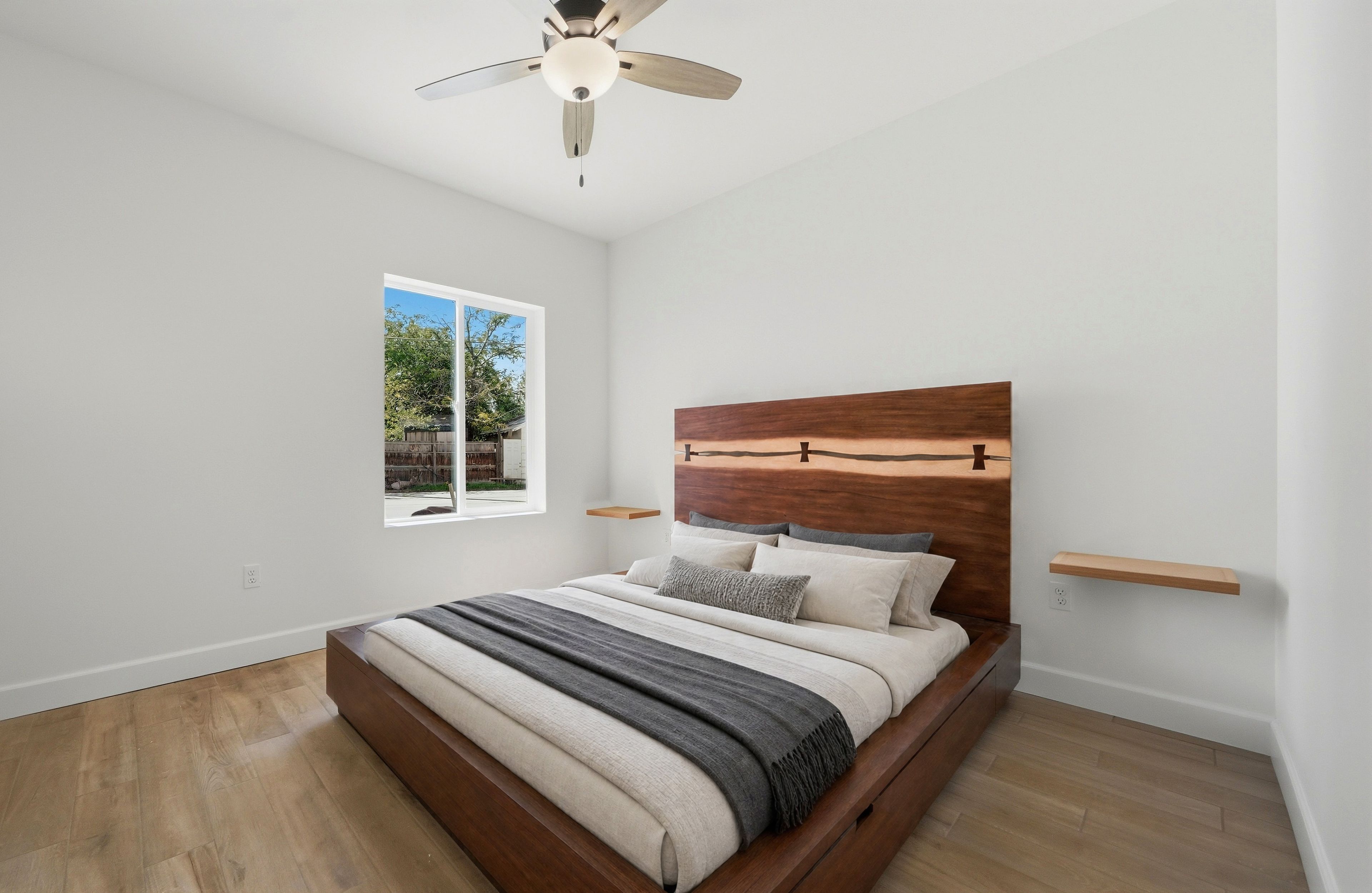 Une chambre à coucher avec une tête de lit en bois, un lit avec plusieurs oreillers, une fenêtre et un ventilateur de plafond.