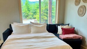 A bed with white bedding, a dark-colored sofa, and a patterned rug.