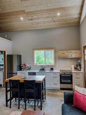 Eine moderne Küche mit Holzschränken, ein Essbereich mit Tisch und Stühlen sowie ein Blick durch ein Fenster.