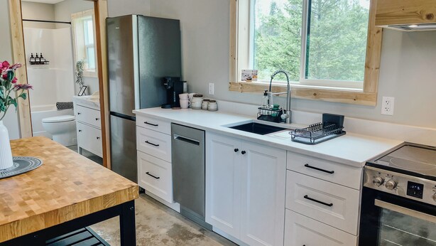 A modern kitchen with white cabinetry, a stainless steel refrigerator, a built-in oven, and a window providing natural light.