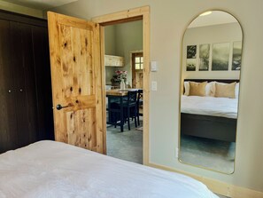A bedroom with a wooden door, a bed, a mirror, and a view into a dining area.