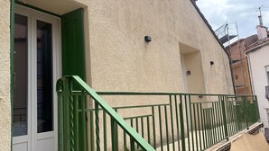 Un edificio con barandal de metal verde, una puerta con contraventanas verdes y una pared con textura.