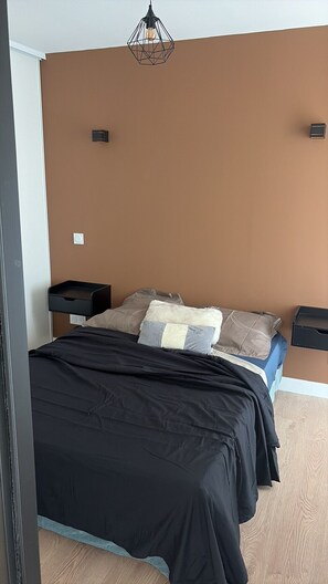 A bedroom with a bed, two bedside tables, a wall-mounted light fixture, and a power outlet. - Tout à pied:plage, commerces et gare (Banyuls-sur-Mer)