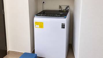 A compact refrigerator in a corner with a blue stool beside it.