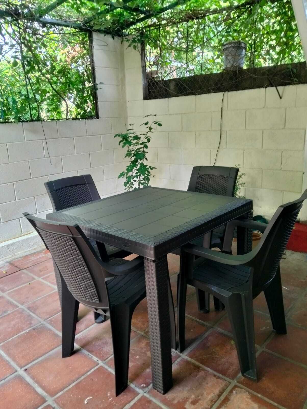 Une terrasse extérieure avec une table et des chaises, entourée d’un mur blanc et de verdure.