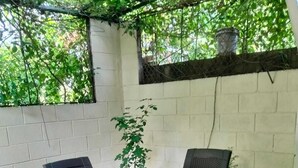 Un patio al aire libre con una mesa y sillas, rodeado por un muro blanco y follaje.