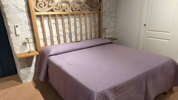 Un dormitorio con estructura de cama de madera, pared blanca, puerta blanca y ventilador de techo.