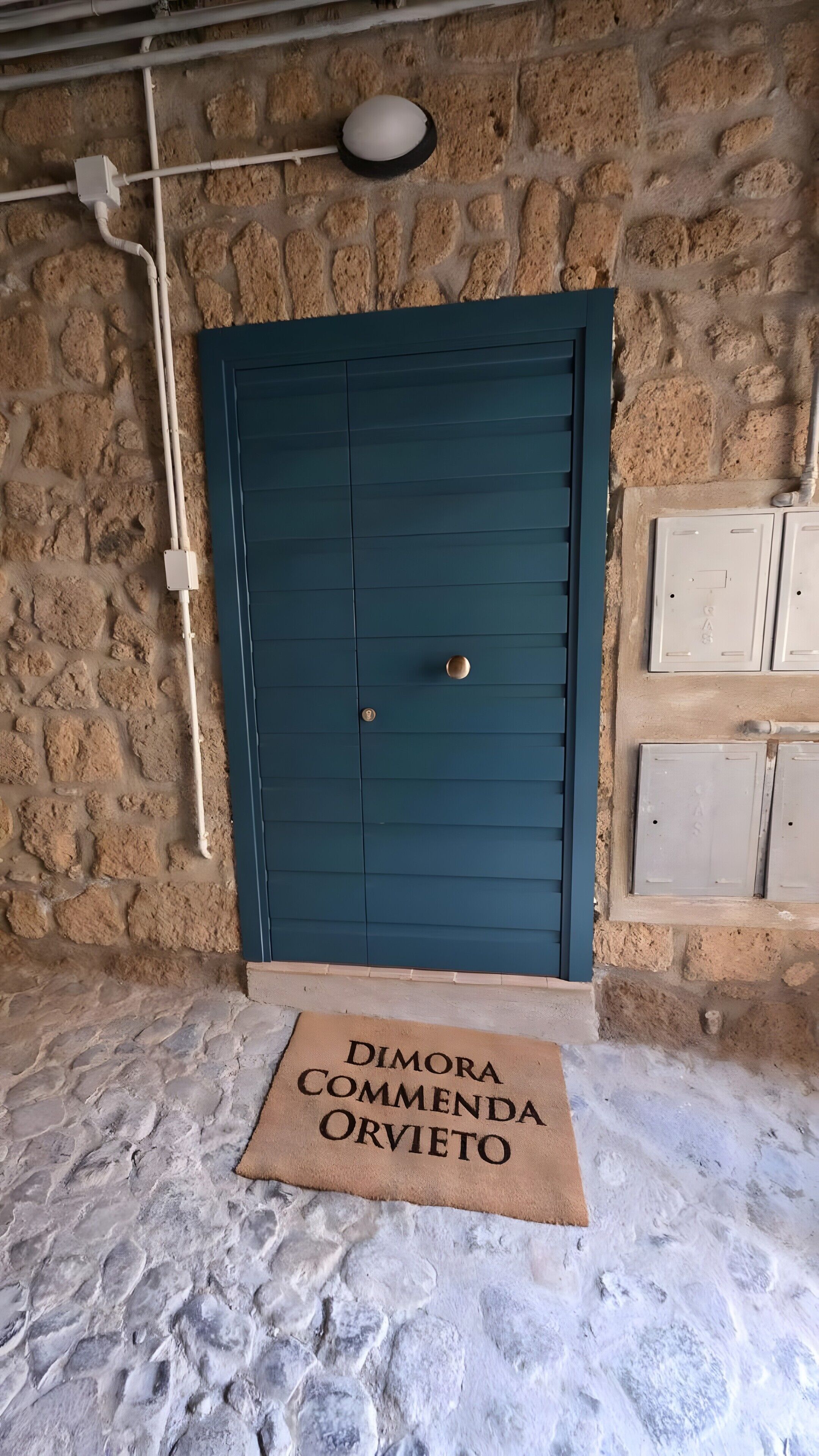 Un muro de piedra con una puerta azul, un felpudo y una lámpara sobre la puerta.
