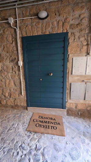Un muro de piedra con una puerta azul, un felpudo y una lámpara sobre la puerta.