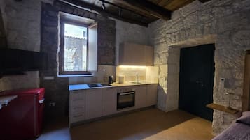 A compact kitchen with a window, a sink, a stove, and a red appliance.