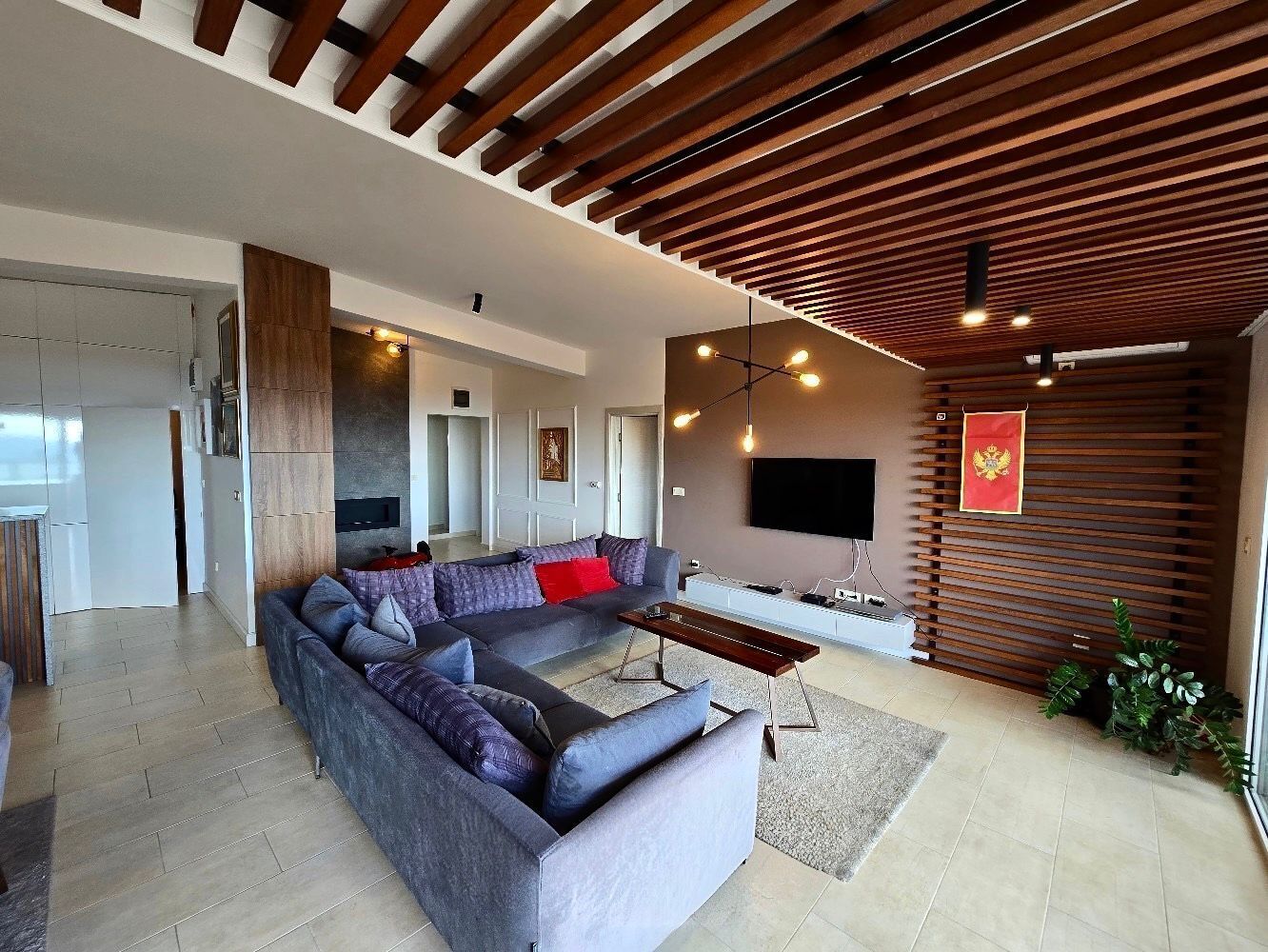 A modern living room with a sectional sofa, a flat-screen TV, and a wooden ceiling.