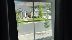 Vista pela janela de uma área residencial, com casas, uma rua e uma montanha ao fundo.