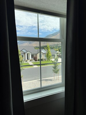 Blick aus dem Fenster auf eine Wohngegend mit Häusern, einer Straße und einem Berg im Hintergrund.