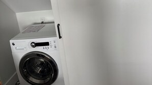 Uma máquina de lavar compacta e branca, fixada na parede, em uma lavanderia pequena com piso estampado.