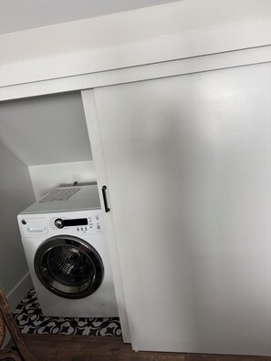 Eine kompakte, weiße, an der Wand befestigte Waschmaschine in einem kleinen Waschraum mit gemustertem Boden.
