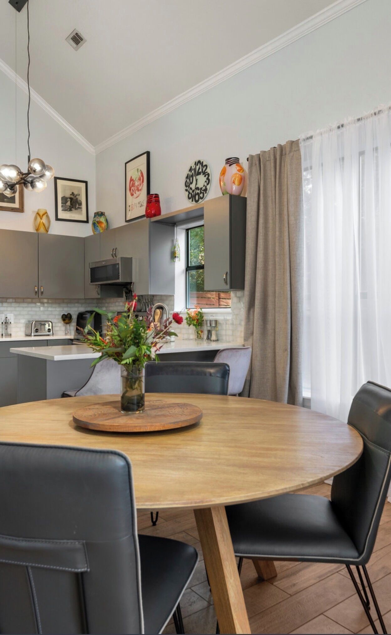 Una cuina moderna amb una illa central, armaris grisos i una zona de dinar amb una taula rodona i caires.