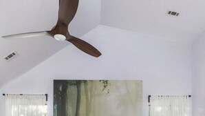 Ein Schlafzimmer mit einem großen Bett, einem Holz-Kopfbrett, einem Deckenventilator und einem Waldgemälde an der Wand.