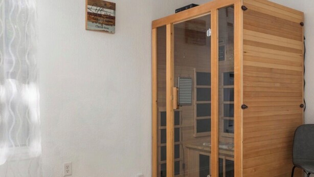 Ein Zimmer mit Deckenventilator, einem Holzkabinett mit Glastüren, einem Stuhl und einem Fenster mit durchsichtigen Vorhängen.