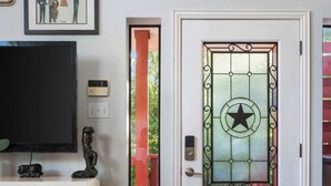 Ein modernes Interieur mit einer weißen Tür mit Sternenmuster, einem Flachbildfernseher auf einem weißen Schrank und einem senkrechten, roten Fenster.