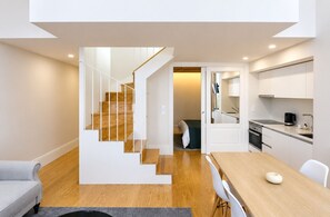 A modern apartment with a wooden staircase, a dining area with a wooden table and chairs, a kitchen with white cabinets, and a small bedroom with a bed and a nightstand. - D&S - Mercado dos Poetas Porto (Porto)