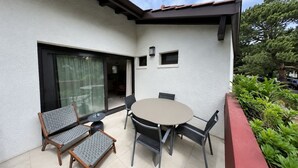 Eine Terrasse mit rundem Tisch und Stühlen, einer Schiebetür aus Glas und einem kleinen Fenster mit einer Lampe.