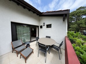 Eine Terrasse mit rundem Tisch und Stühlen, einer Schiebetür aus Glas und einem kleinen Fenster mit einer Lampe.