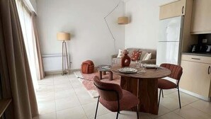 Ein moderner Essbereich mit einem Holztisch, vier Stühlen, einer Couch, einer Lampe und einem Kühlschrank im Hintergrund.