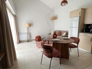 Ein moderner Essbereich mit einem Holztisch, vier Stühlen, einer Couch, einer Lampe und einem Kühlschrank im Hintergrund.