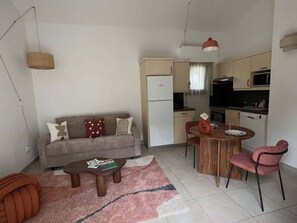 A compact living space with a sofa, coffee table, dining table, and chairs. A kitchenette with a refrigerator, microwave, and stove is visible. - Residence Océan&Foret: T2 appartement, 1 chambre avec terrasse (Anglet)